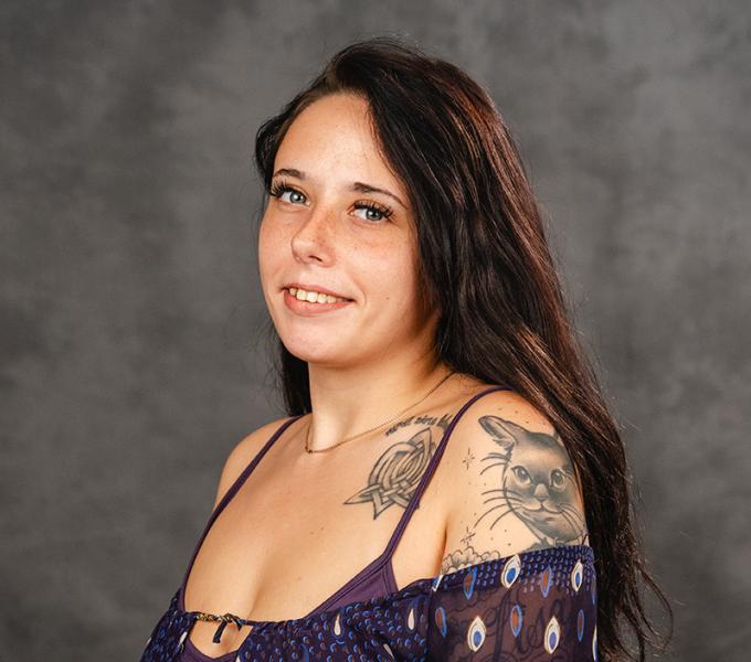 A woman with long dark hair smiling in a purple top.
