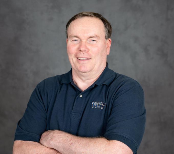 Headshot of man in a dark navy polo shirt with his arms crossed.