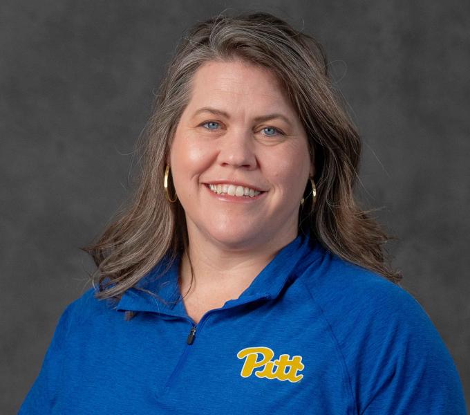 Headshot of a smiling woman with mousy brown hair in a blue Pitt-branded quarter-zip shirt.