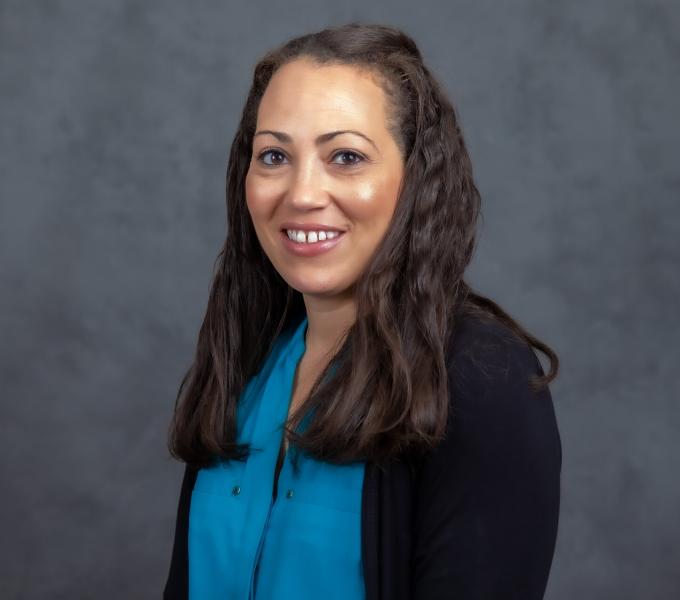 Headshot of smiling woman in a blue shirt with a black cardigan.