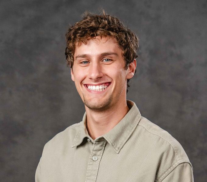 Headshot of a smiling man with short, curly hair in a light green shirt.