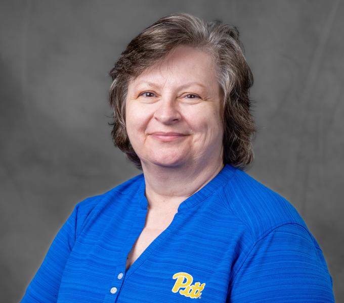 Headshot of a smiling woman with short gray hair in a blue Pitt shirt.