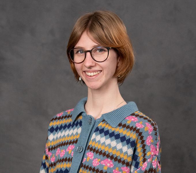 A woman with short brown hair and glasses smiling in a striped sweater.