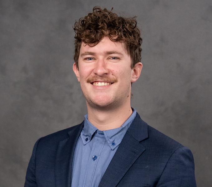 A man with short curly hair smiling in a navy suit.