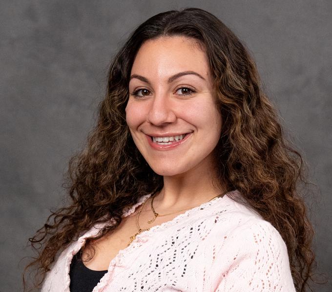 A woman with long curly hair smiling in a pink sweater.