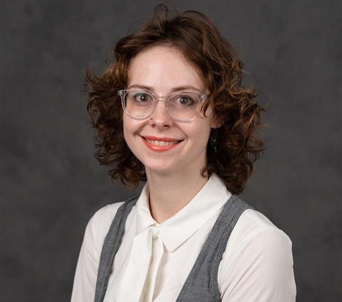 A white woman with short curly hair smiling wearing glasses and a white blouse.