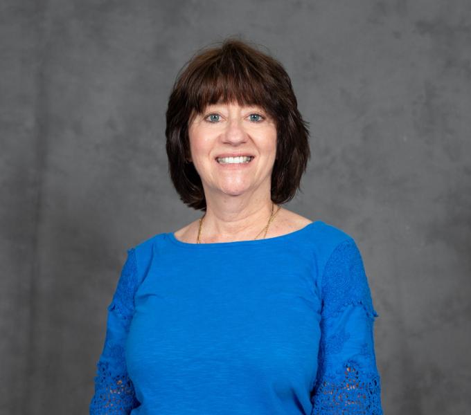 Headshot of smiling woman in long sleeved blue blouse with short brown hair and bangs.