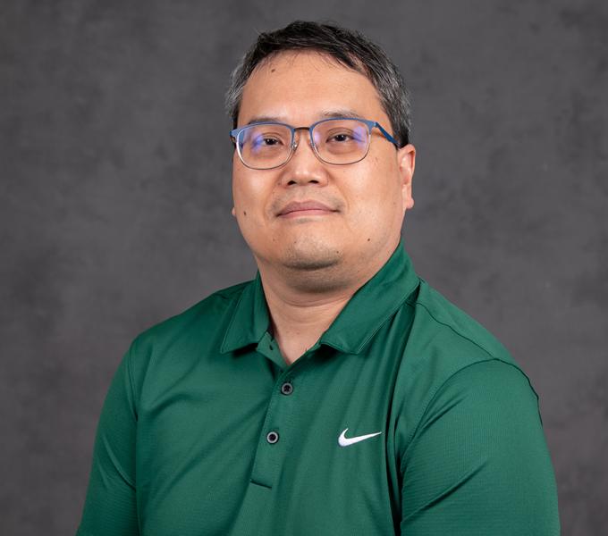 A man with short dark hair and glasses in a green polo shirt.