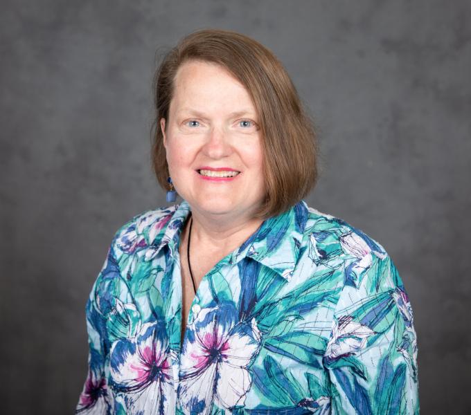 Headshot of smiling woman with a light brown bob haircut and tropical blue-green blouse.