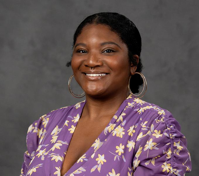 Photo of a woman with dark hair in a bun smiling in a purple floral top.