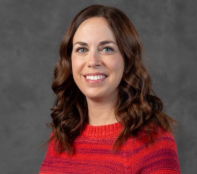 Headshot of a smiling woman with brown hair in loose waves wearing a rich red and pink striped sweater.