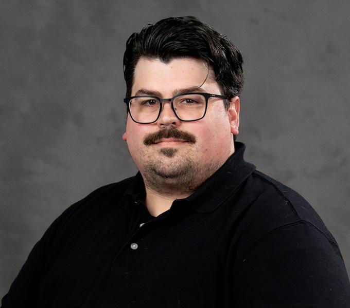 Photo of a man with dark hair and a mustache in a black polo shirt.