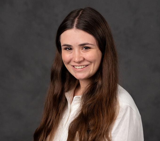 A woman with long dark hair smiling in a white button up top.