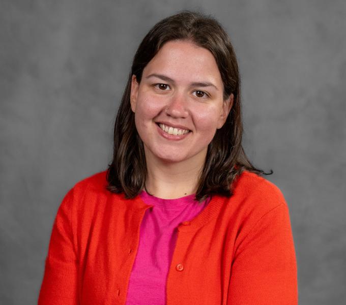 Headshot of a smiling brunette woman in a hot pink shirt and bright orange cardigan.