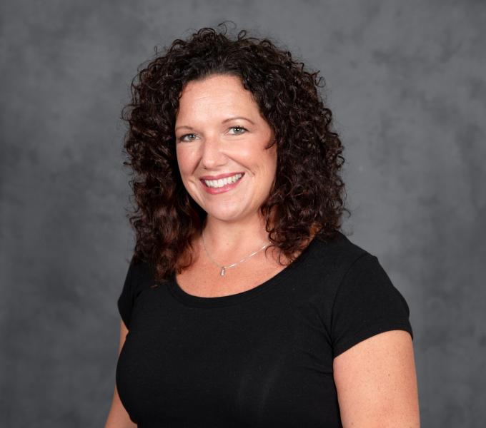 Headshot of smiling woman in a black short sleeve shirt with dark brown curly hair.