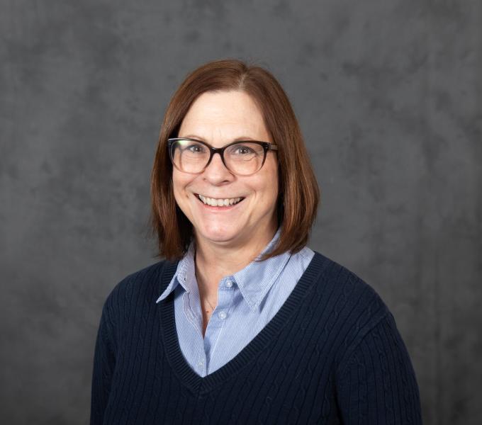 Headshot of smiling woman in cat eye glasses, a light blue button down shirt, and navy blue sweater.