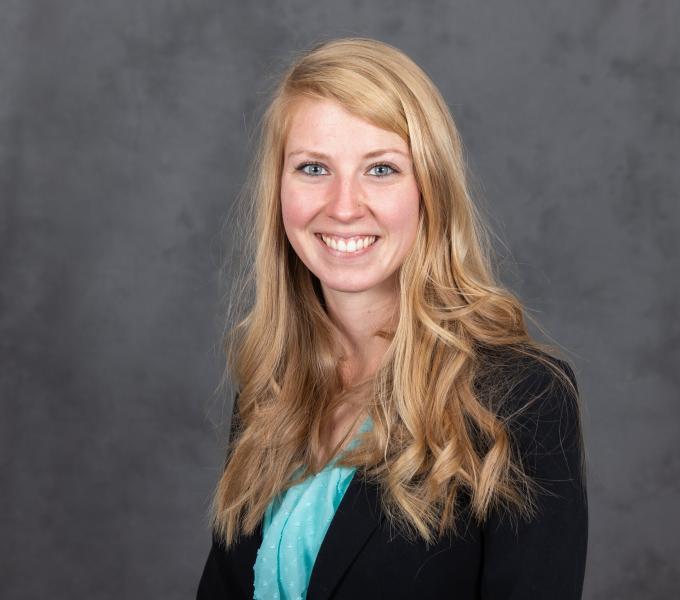 Headshot of smiling woman with long blonde hair in a bright teal shirt and black blazer.