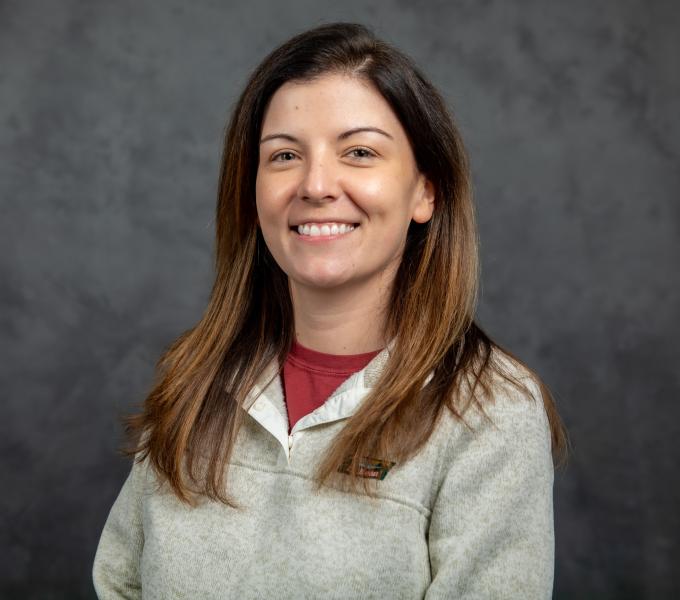 Headshot of smiling woman in a gray fleece quarter zip sweatshirt over a maroon shirt.