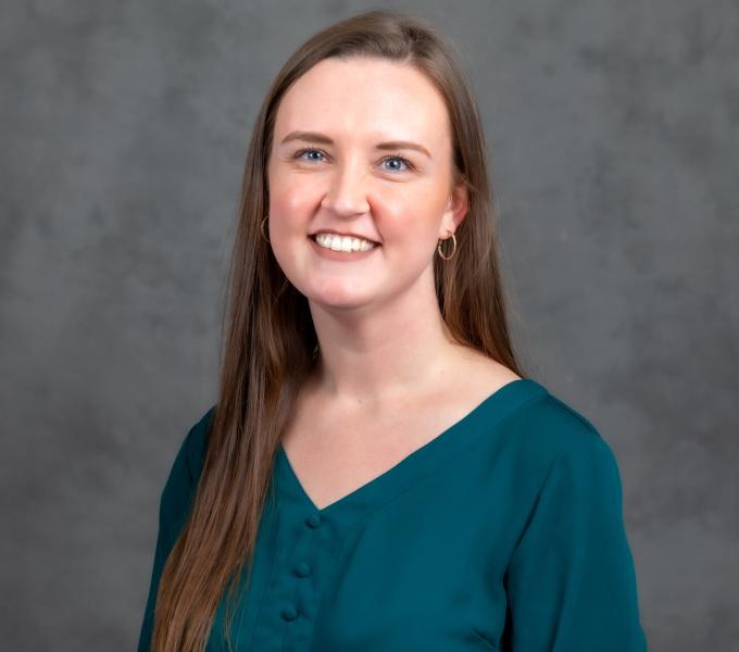 Headshot of smiling woman with long straight brown hair in a turquoise v neck shirt.