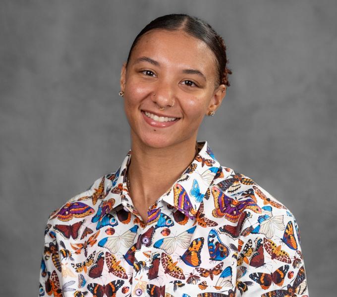 Headshot of a smiling young person with pulled-back dark hair in a butterfly-printed polo shirt.