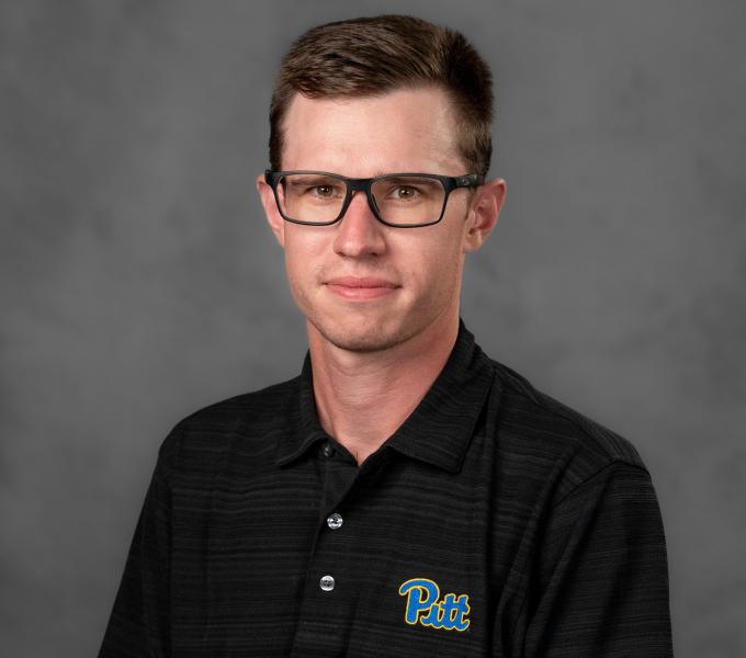 Headshot of a man in a charcoal and blue Pitt branded polo shirt.