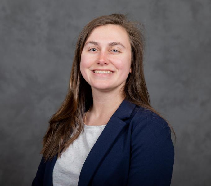 Headshot of smiling young woman with long light brown hair in a white shirt and navy cardigan.