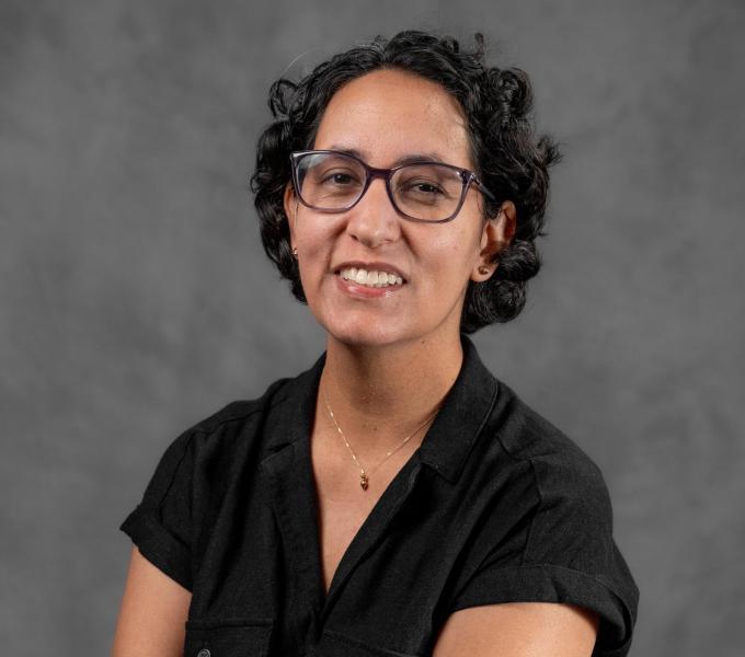 Headshot of a smiling woman with short black hair in glasses and a black shirt.