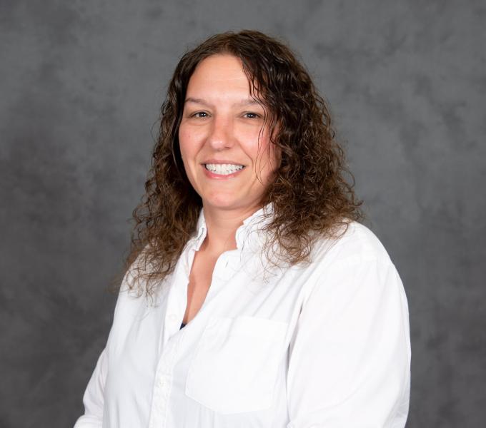 Headshot of woman with curly medium brown hair in a white long-sleeve shirt.