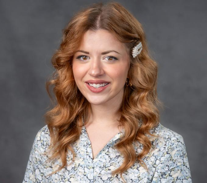 Headshot of a woman with curled strawberry blonde hair in a light-colored floral button down shirt and pearl hair clip.