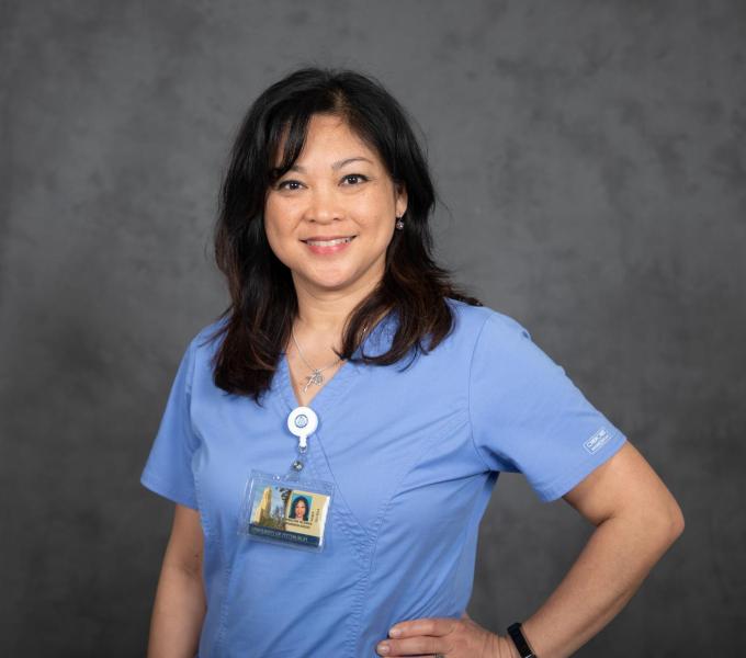 Headshot of smiling woman with dark hair in blue short-sleeved scrubs with an ID lanyard.