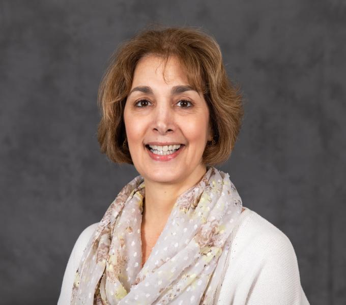 Headshot of smiling woman in a white shirt and cream-colored polka dot scarf.