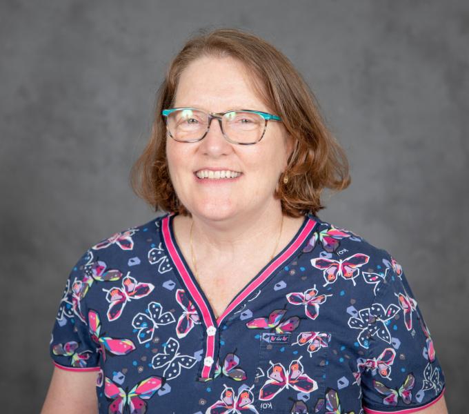 Headshot of smiling woman in dark navy scrubs with pink trim and butterfly print.
