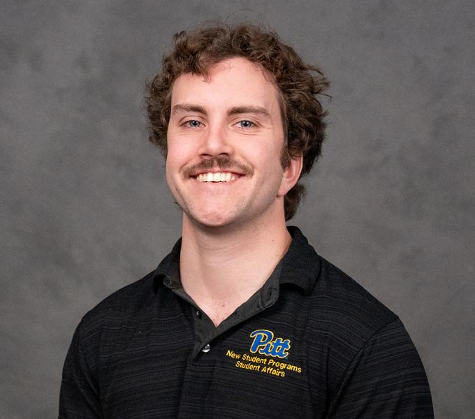 A man with short curly hair and a mustache smiling in a black polo shirt.