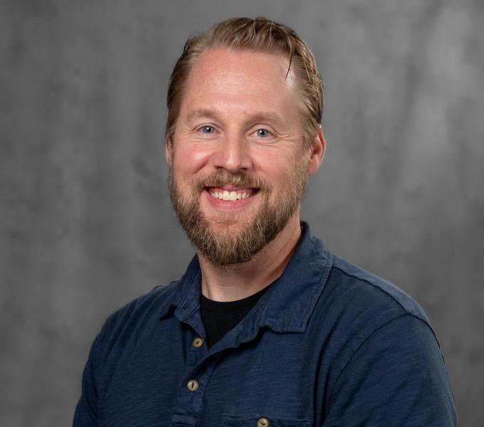 Headshot of a smiling bearded man in a navy polo shirt.