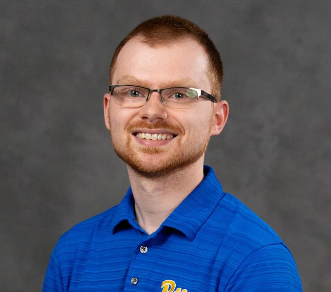 A man with short hair and glasses smiling in a blue polo.