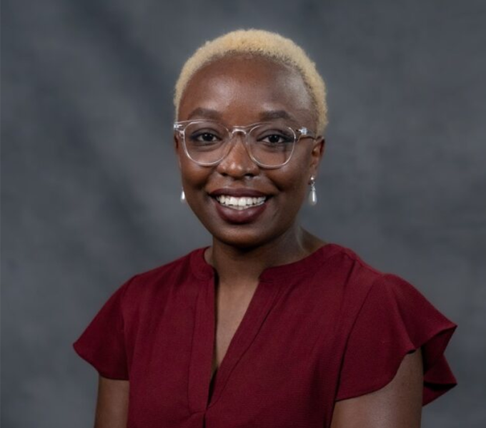 A woman with short blonde hair and glasses smiling in a red blouse.