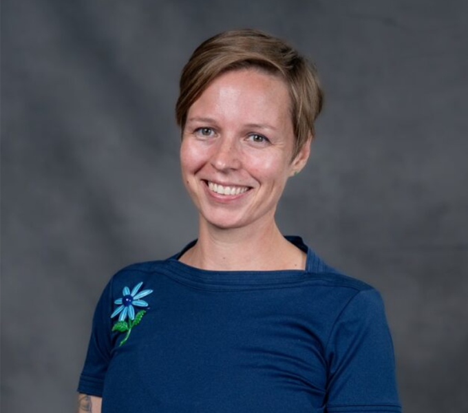 A woman with short brown hair smiling in a blue short sleeve top.