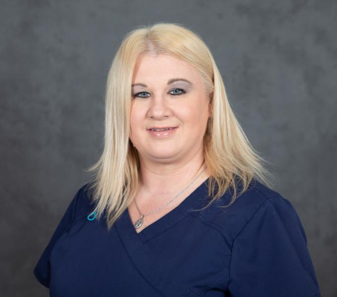 Headshot of blonde woman in a dark turquoise blue shirt.