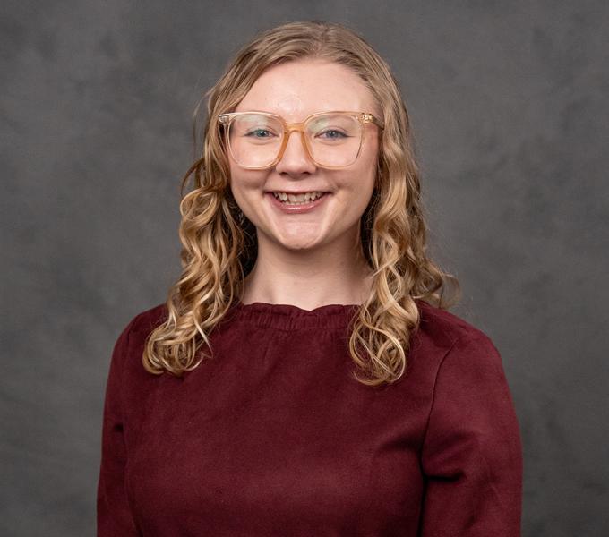 A woman with blonde curly hair and glasses smiling in a red top.