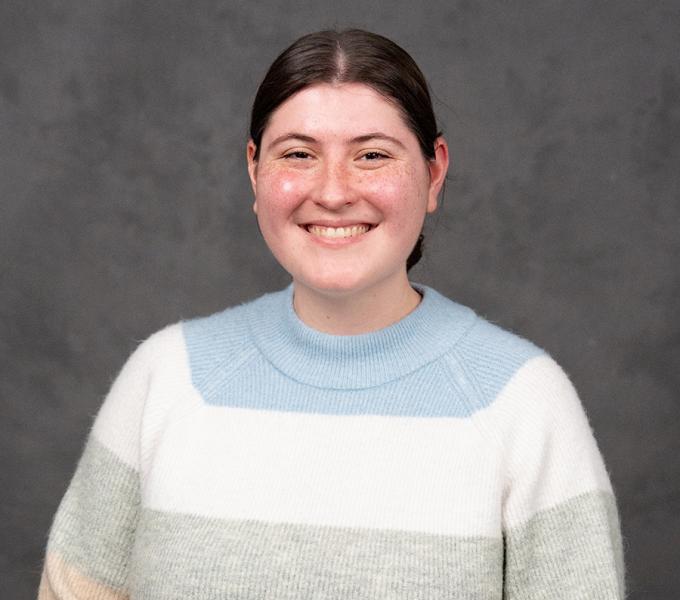 A woman with dark hair tied back smiling in a pastel sweater.