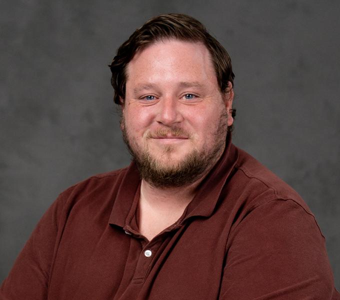 Photo of a man with dark short hair smiling in a brown polo shirt.