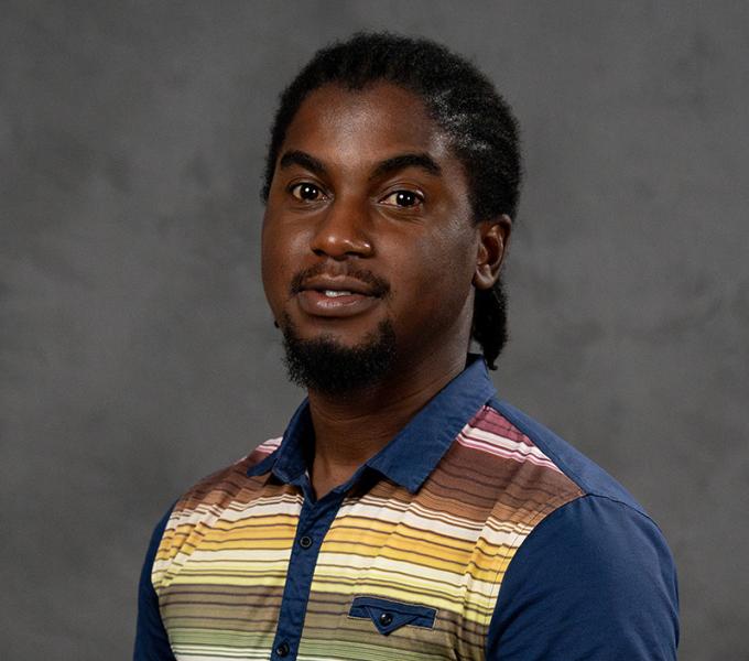 A man with braided hair in a striped polo shirt.