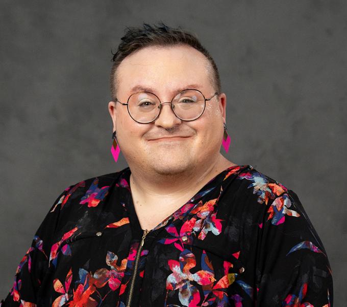 Photo of a person with short hair smiling in a black and pink floral top.
