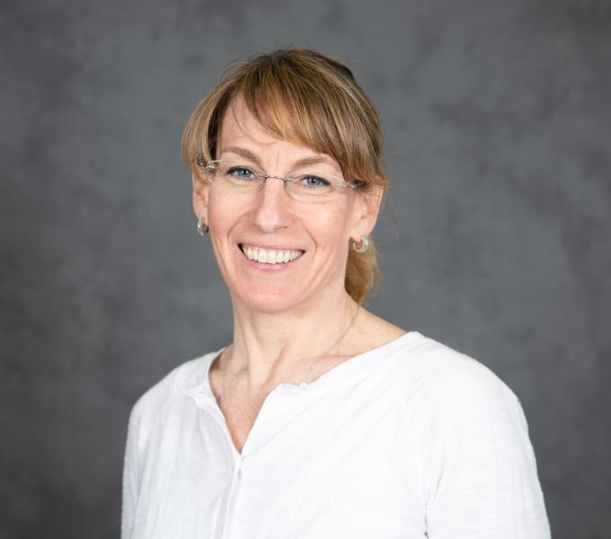 Headshot of smiling blonde woman with bangs and rimless glasses in a white blouse.