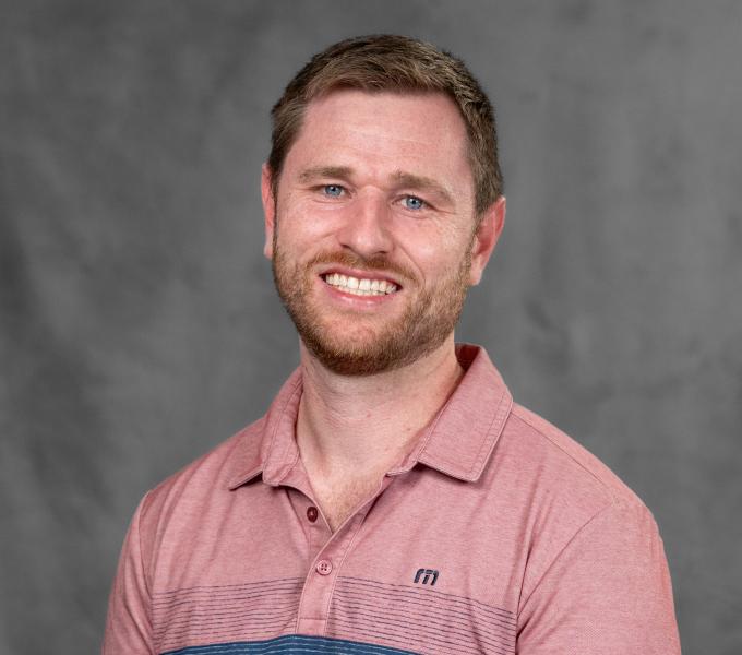 Headshot of a smiling man in a pink and navy polo shirt.