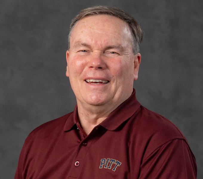 Headshot of a laughing man in a maroon Pitt-branded collared shirt.