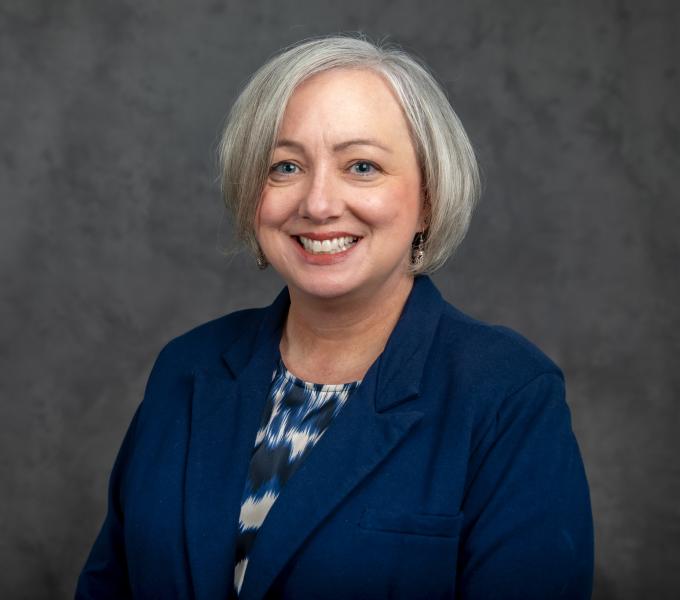 Headshot of a smiling woman with short silver hair in a navy blue blazer.