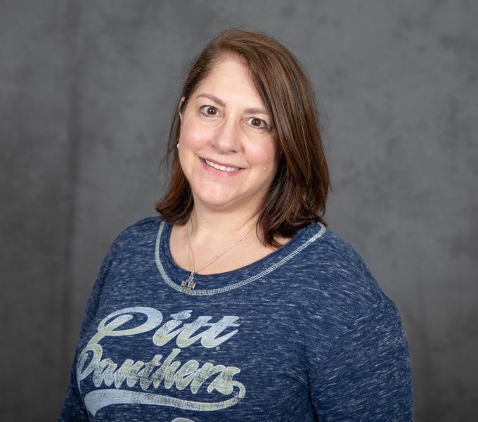 Headshot of smiling woman with short brown hair in a heather blue Pitt Panther sports shirt.