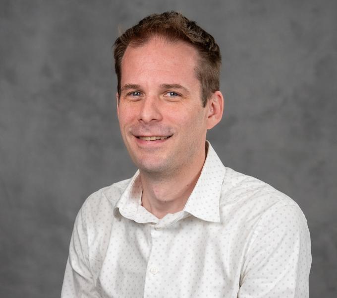 Headshot of a smiling man in a patterned white button down shirt.