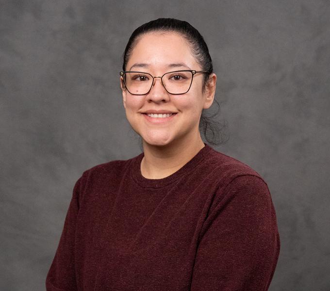A woman with dark hair and glasses smiling in a red sweater.